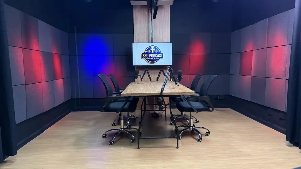 Mesa central do estúdio de podcast OFBOX com quatro cadeiras, microfones articulados e iluminação cênica vermelha e azul.
