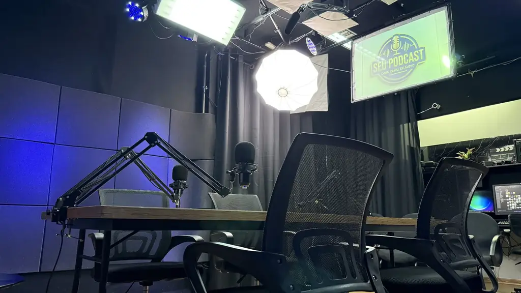 Bastidores do estúdio OFBOX mostrando a mesa de podcast, iluminação profissional e monitor com identidade visual da gravação.