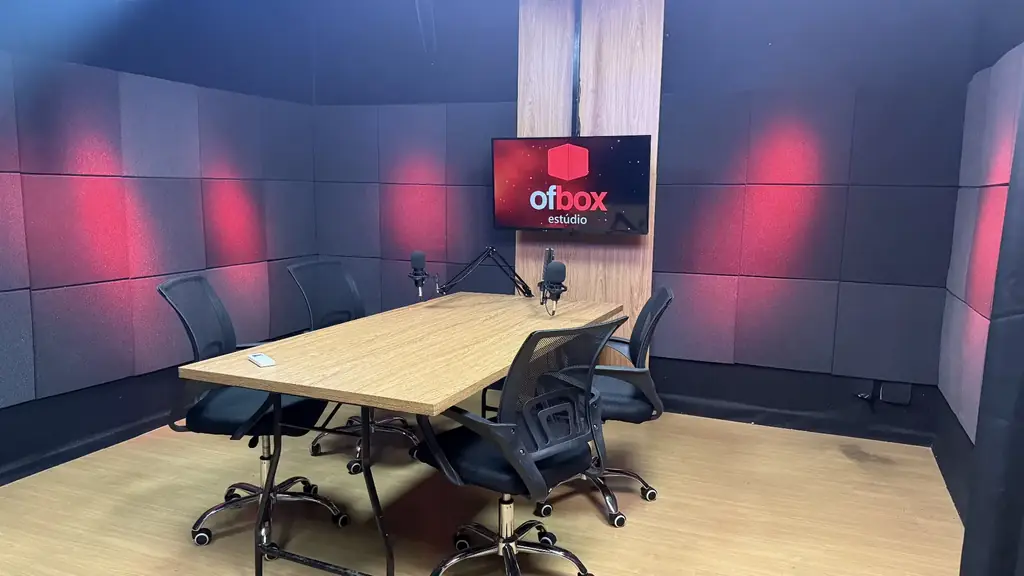 Estúdio OFBOX em perspectiva lateral com mesa de podcast, cadeiras giratórias e monitor com a marca do estúdio.