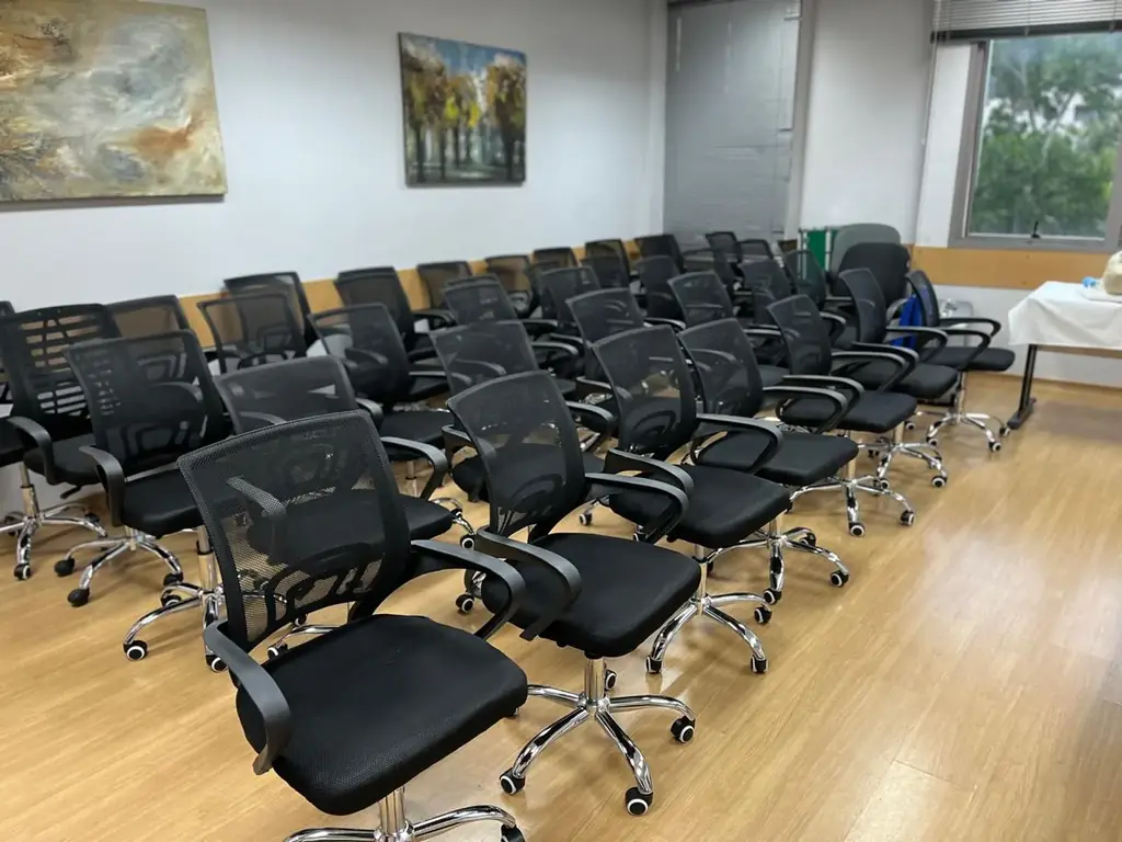 Sala de aula OFBOX montada em formato auditório com cadeiras giratórias pretas enfileiradas e piso de madeira clara.