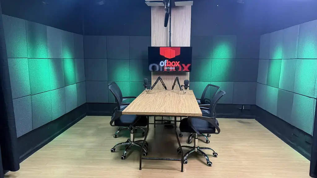 Vista frontal do estúdio OFBOX com iluminação verde, painel acústico e estrutura preparada para gravação de podcast.