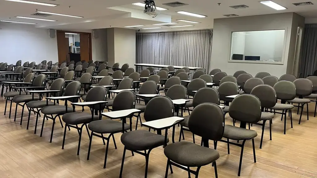 Auditório OFBOX em formato sala de treinamento com cadeiras universitárias acolchoadas, piso de madeira, projetor e cabine técnica ao fundo.